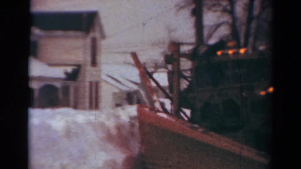 1954 Toledo frame showing the snowplow continuing down a snowy residential street past houses and bare winter trees.