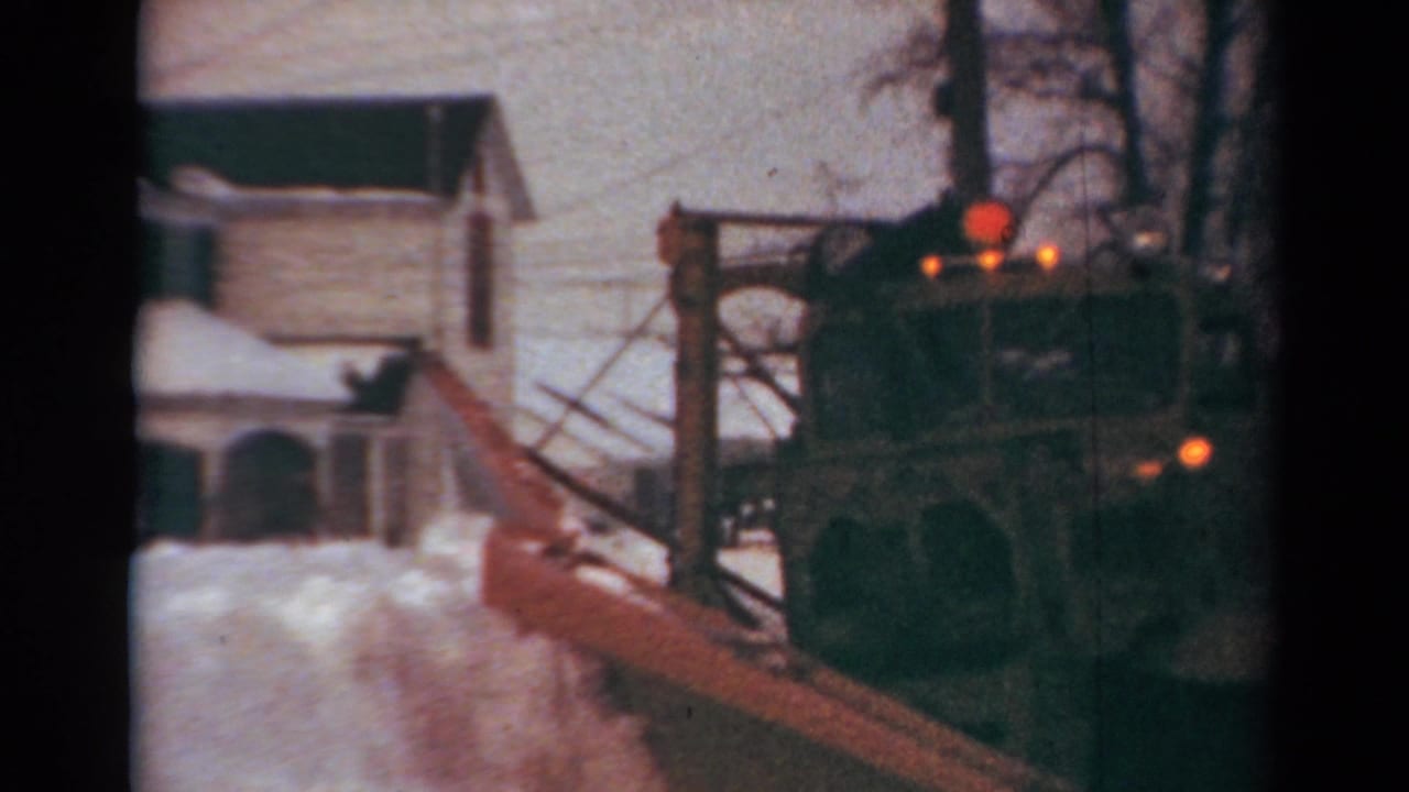 1954 Toledo home-movie frame showing a large red plow moving snow past residential houses in winter.
