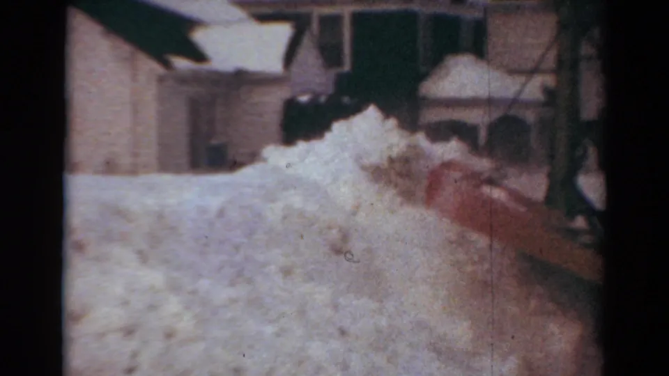 The red plow blade presses into a tall snowbank on a Toledo residential street, with house exteriors behind it.