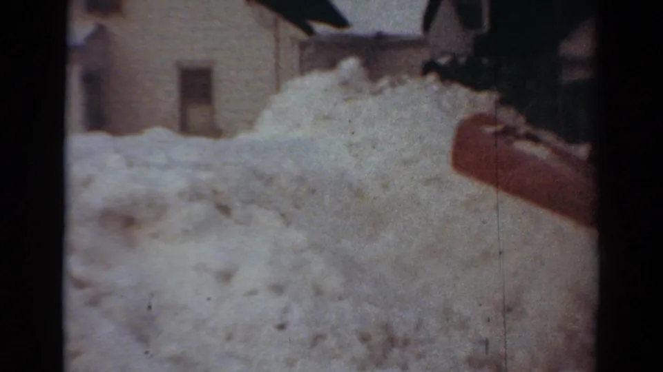 Heavy snow fills the foreground while the red plow blade continues past residential buildings in the 1954 Toledo footage.