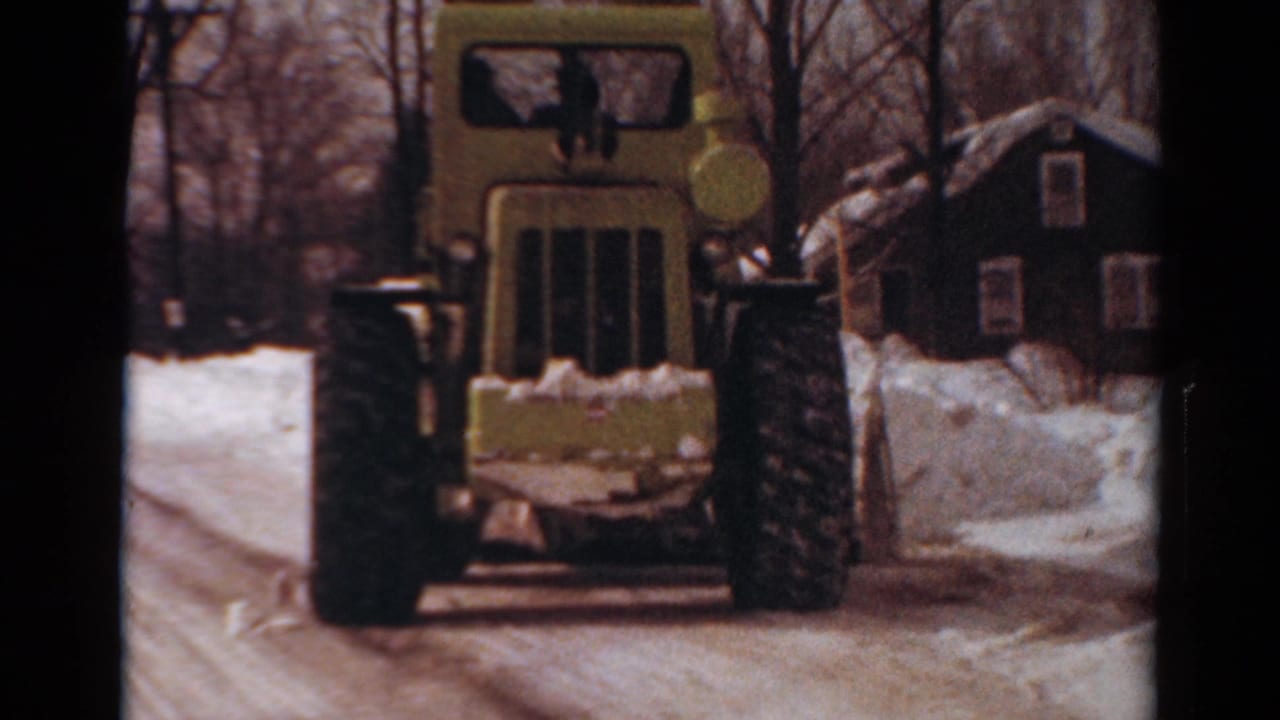 Yellow snow-clearing machine faces the camera on a snowy residential road.