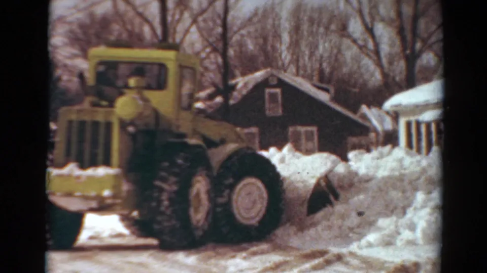 1954 Toledo home-movie frame showing the plow close to camera as it works past houses and piled winter snow.