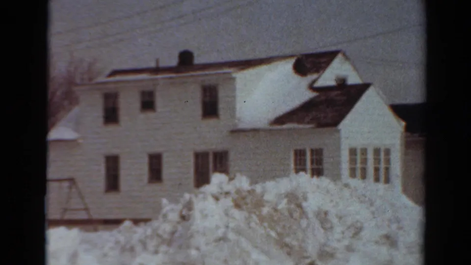 1954 Toledo winter frame showing a white residential building with a side extension, multiple windows, bare trees, utility lines, and high snowbanks in the foreground.