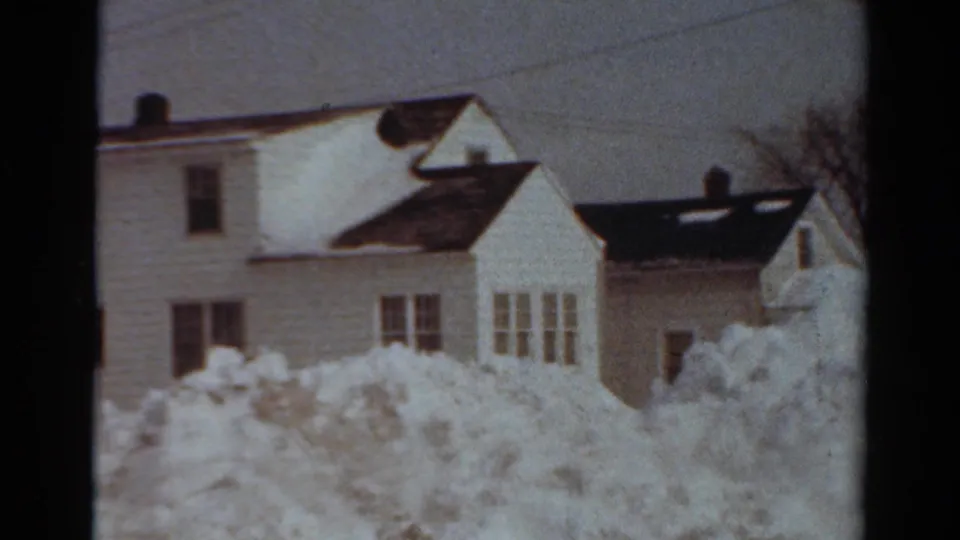 Snow-covered residential houses in Toledo, Ohio, with deep drifts, dark roofs, and a bare winter tree.
