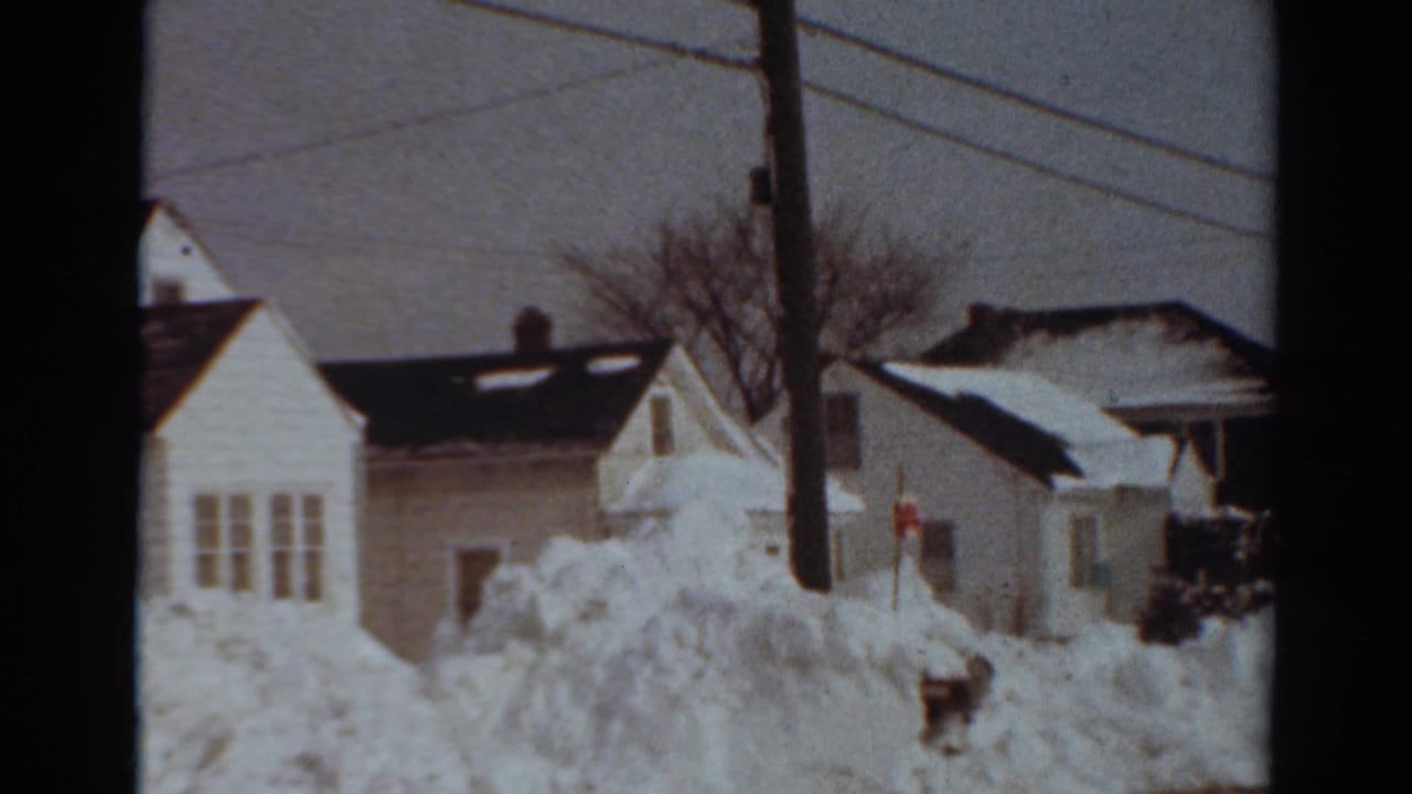 1954 Toledo home-movie frame showing snow-buried suburban houses, overhead wires, a utility pole, and deep winter drifts.