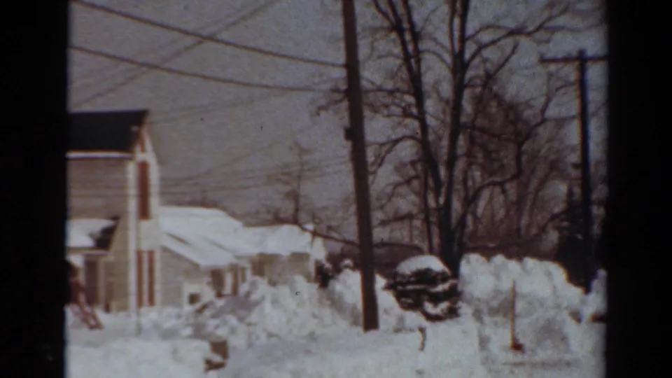 1954 Toledo home-movie view across a snowy residential block with houses, tall drifts, bare trees, and utility poles.