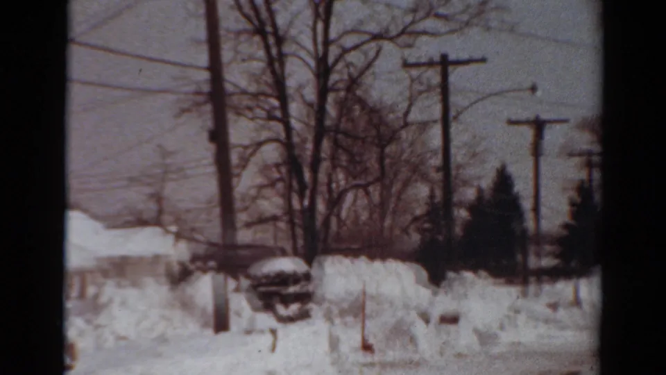 1954 Toledo winter frame showing a quiet snow-covered neighborhood, bare trees, overhead wires, and piled snow along the road.