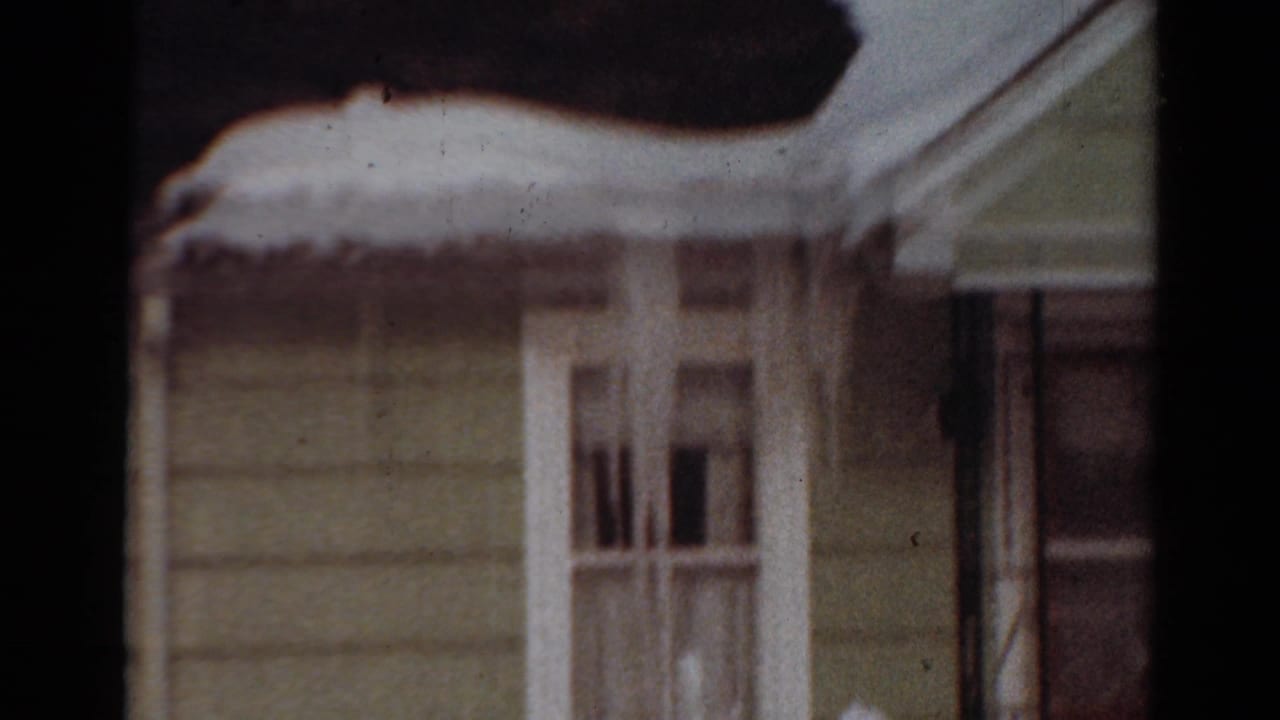 1954 Toledo, Ohio 8mm frame showing a snow-covered house exterior with pale siding, white window trim, and heavy snow along the eaves.