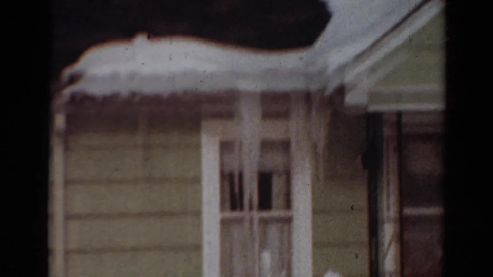 1954 Toledo, Ohio 8mm frame showing a snow-covered house exterior with pale siding, white window trim, and heavy snow along the eaves.