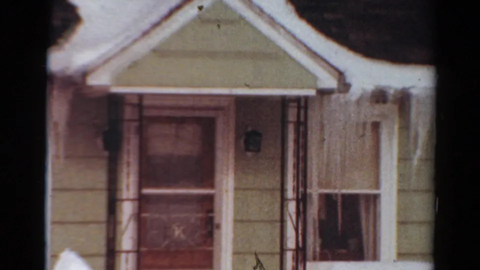 1954 Toledo, Ohio 8mm frame showing a front porch or entry with a storm door, adjacent window, pale siding, and snow accumulated around the roof edge.