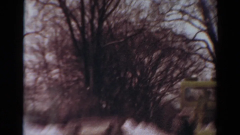 1954 Toledo, Ohio 8mm frame looking past bare winter shrubs toward a snowy street edge, with part of a vehicle or snowplow visible at the right.