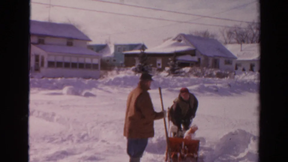 A man with a shovel watches as another works at the snow blower in a snowy 1954 Toledo neighborhood.