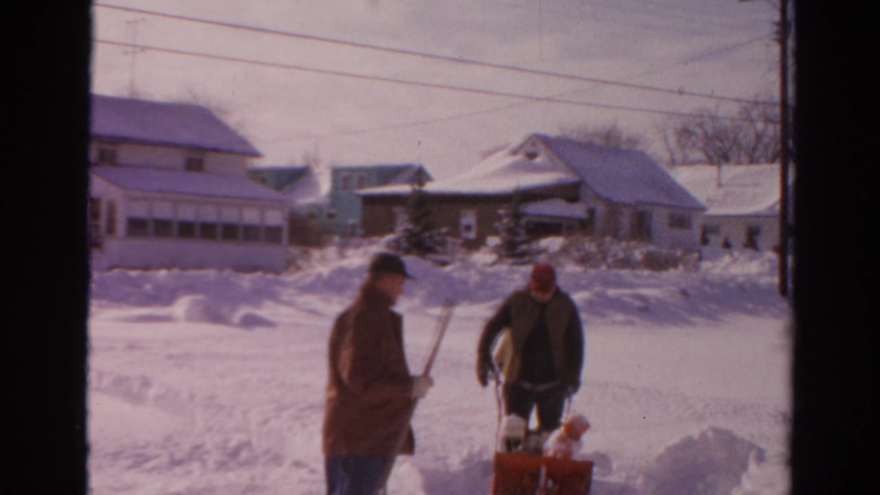 Two men pause beside a red snow blower during snow clearing in a 1954 Toledo residential setting.