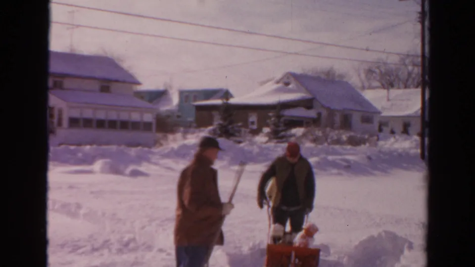 Two men pause beside a red snow blower during snow clearing in a 1954 Toledo residential setting.
