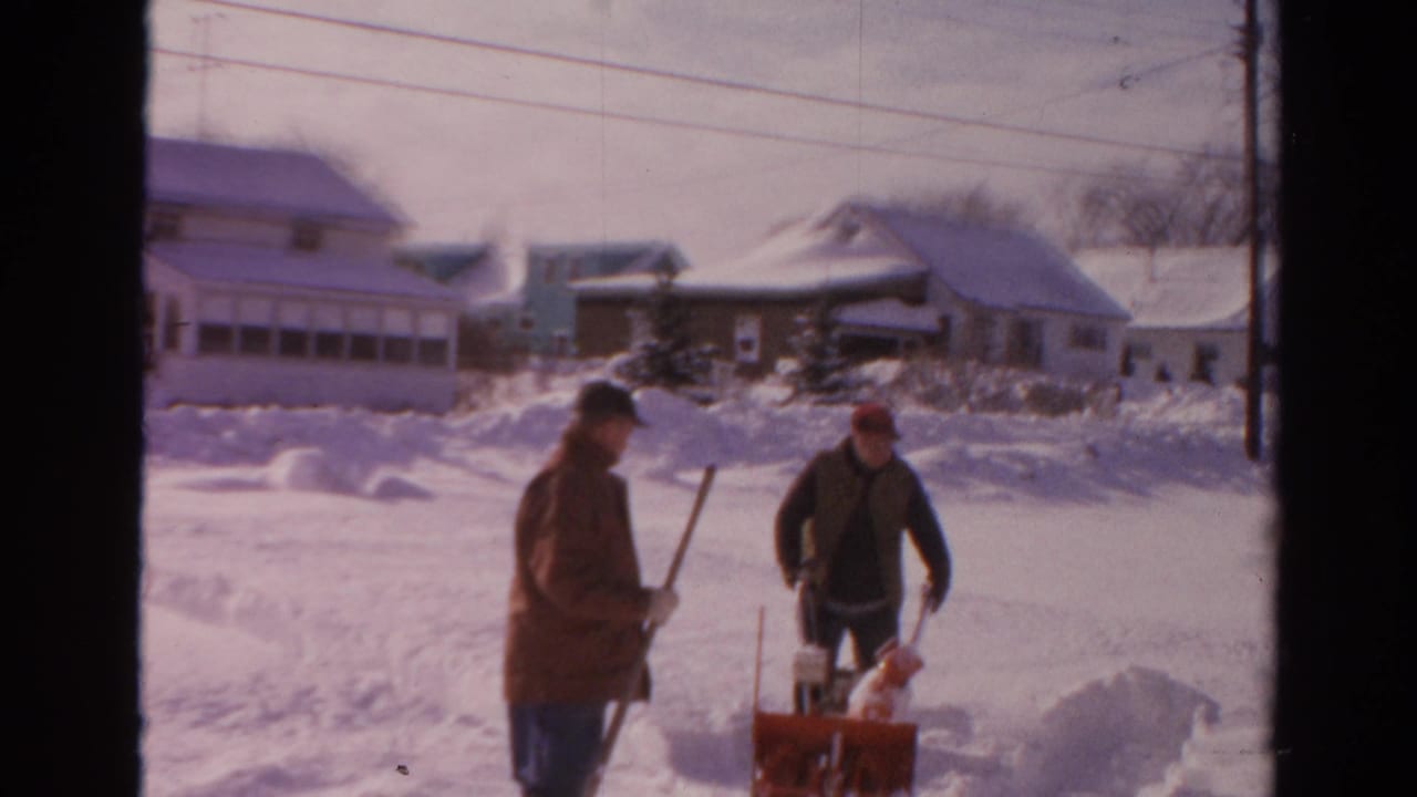 Two men clear snow on a Toledo residential street in supported 1954 8mm footage, with houses and snowbanks behind them.
