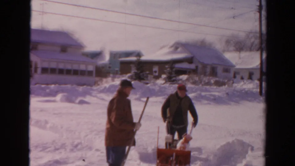 Two men clear snow on a Toledo residential street in supported 1954 8mm footage, with houses and snowbanks behind them.