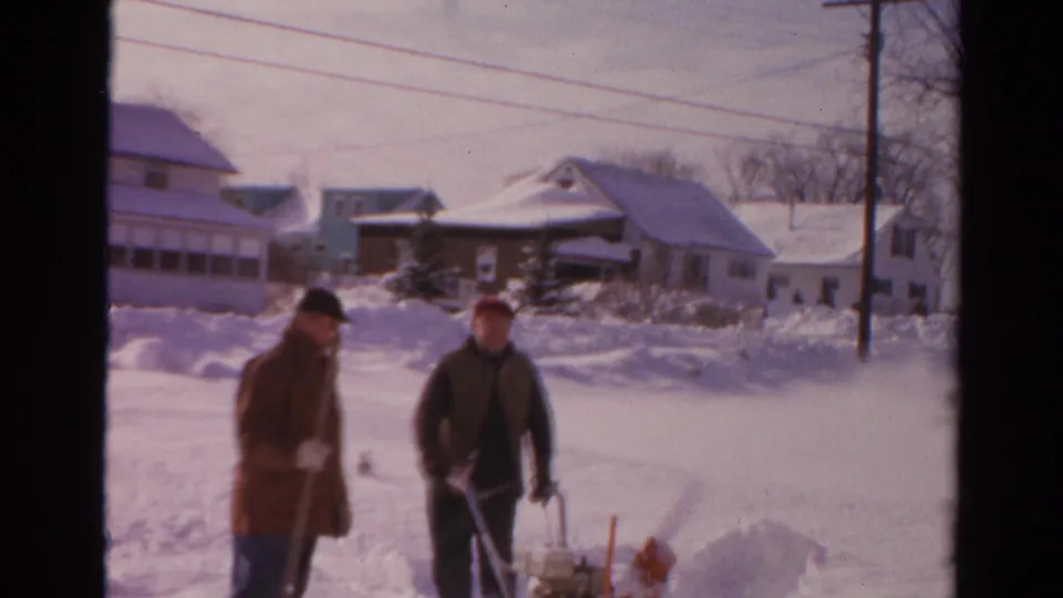 Two men in winter clothing approach the camera during residential snow clearing in supported 1954 Toledo home-movie footage.