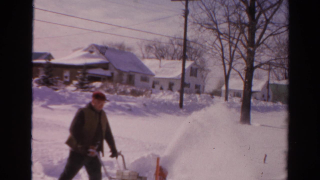 In Toledo, Ohio, 1954 home-movie footage, a man in a red cap operates a snowblower beside snowbanks and houses.