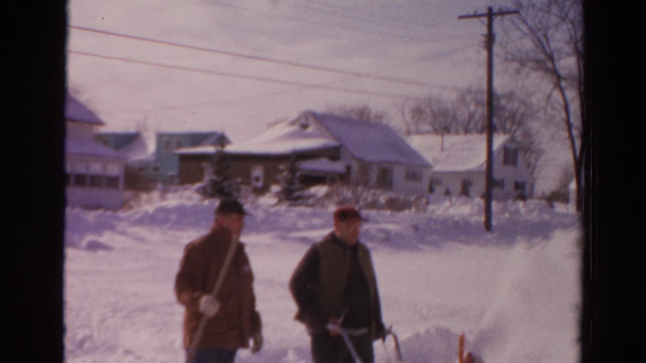 The two men continue past snow-covered homes in Toledo, with a shovel, snowblower, bare trees, and utility lines visible.