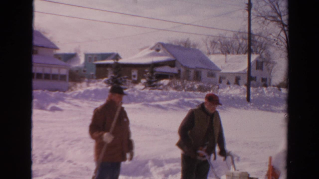 Near the end of the 1954 Toledo clip, one man stands with a shovel while another leans near the snowblower in deep snow.