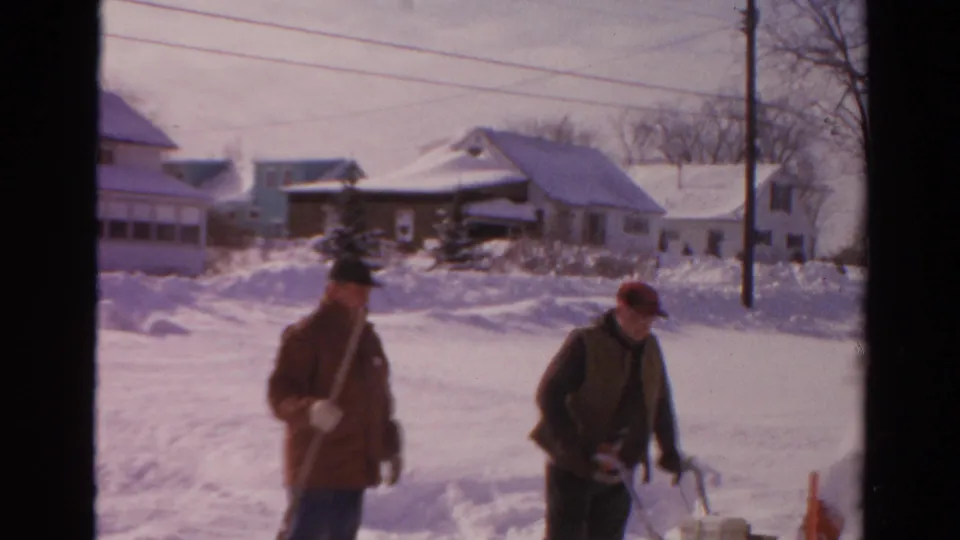 Near the end of the 1954 Toledo clip, one man stands with a shovel while another leans near the snowblower in deep snow.