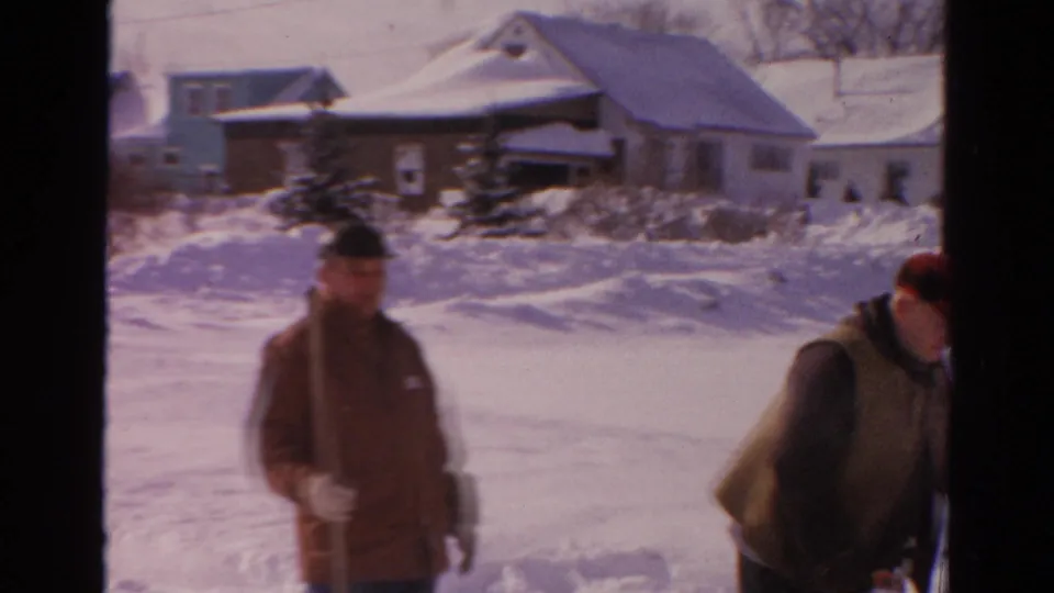 A bundled man stands near snowbanks in a Toledo residential street, with houses and bare trees in the background.