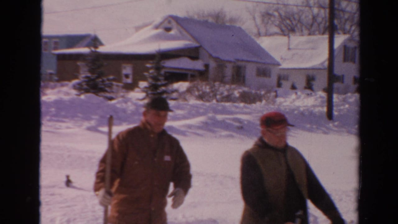 Adult man shovels snow in a snowy Toledo residential neighborhood, with houses and bare trees behind him.