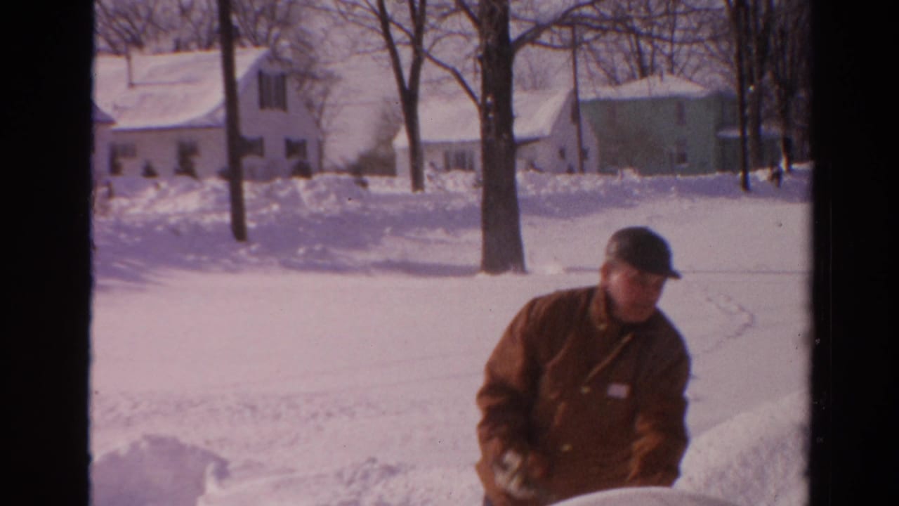Man standing beside a high snowbank in a snowy residential neighborhood.