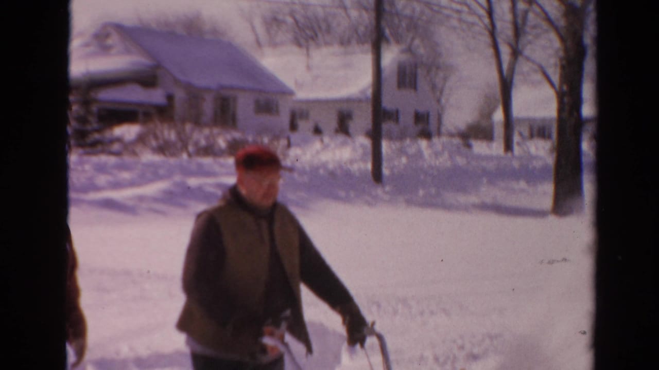 In 1954 Toledo, a man in a red cap and brown vest clears snow near detached houses on a bright winter day.