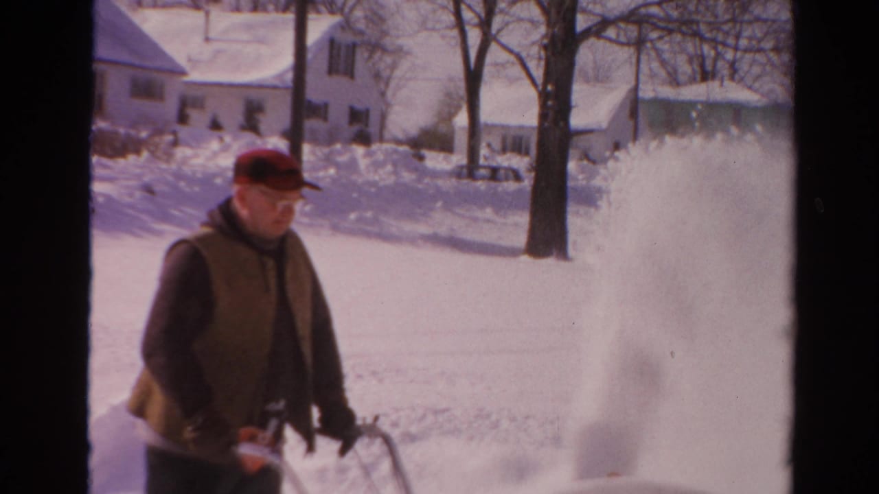 Man guides a snow blower as a plume of snow rises beside him.