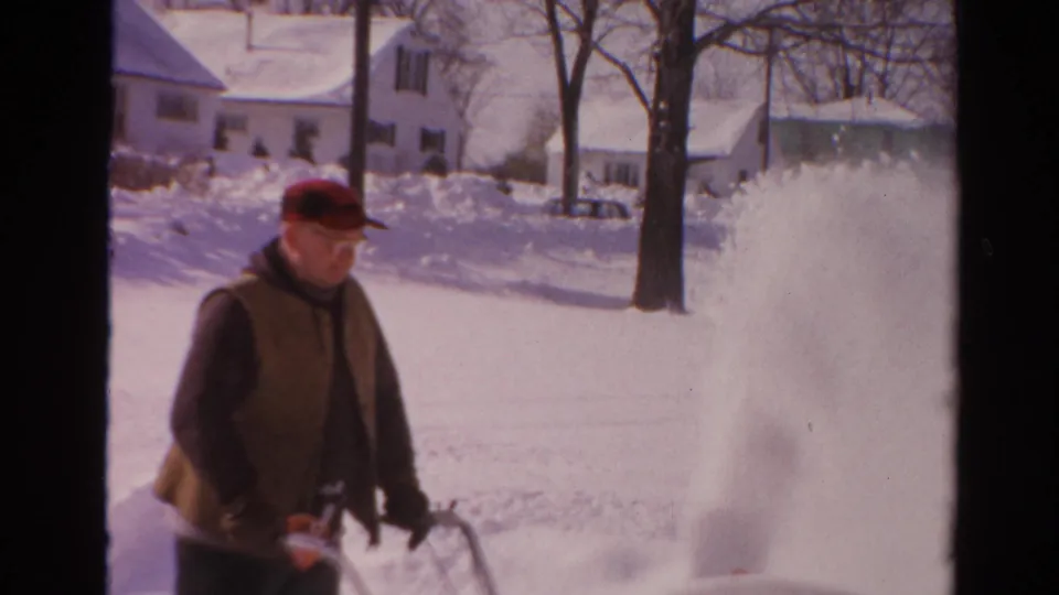 The man moves through the snowy Toledo neighborhood while the snow blower throws a tall white spray into the air.