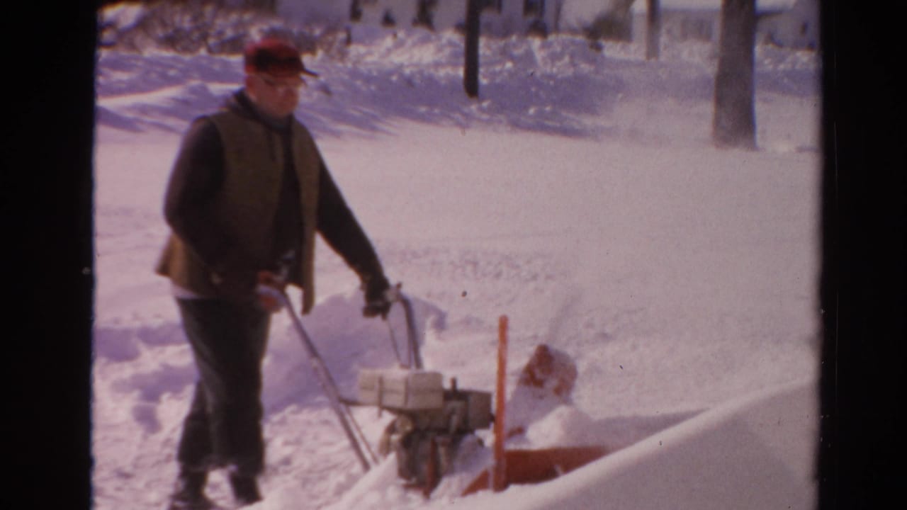 A man operating a snow blower pauses near a shovel and high snowbanks in 1954 Toledo home-movie footage.