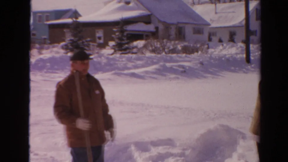 In 1954 Toledo, Ohio, a man in winter clothing stands outdoors beside deep snowbanks and snow-covered suburban homes.