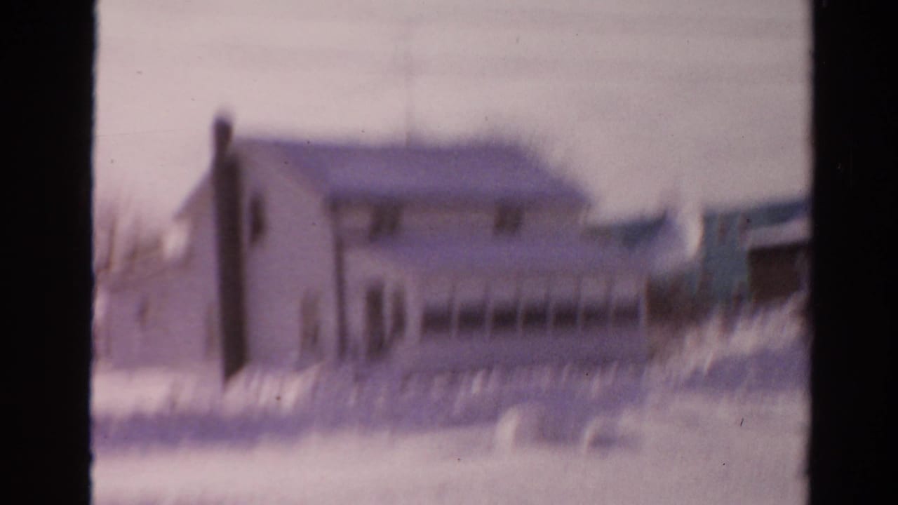 Blurred 1954 Toledo home-movie frame with a house facade and heavy snowbanks filling the foreground.