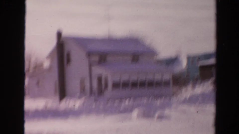 Blurred 1954 Toledo home-movie frame with a house facade and heavy snowbanks filling the foreground.