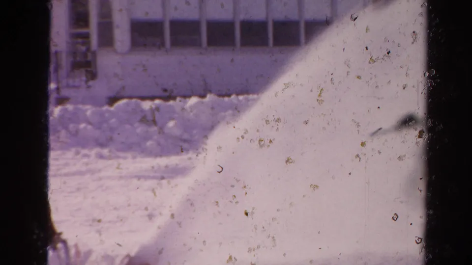 1954 Toledo home-movie frame showing a snowblower plume crossing a snowy driveway near a suburban house.