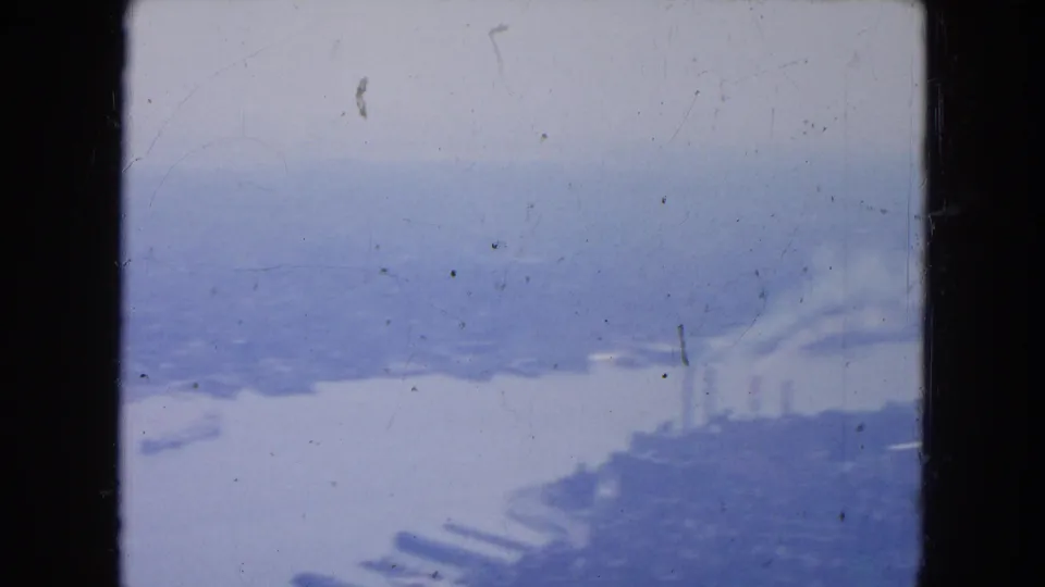 1954 New York aerial view with industrial waterfront structures, piers, smokestacks, and river visible through faded 8mm color.