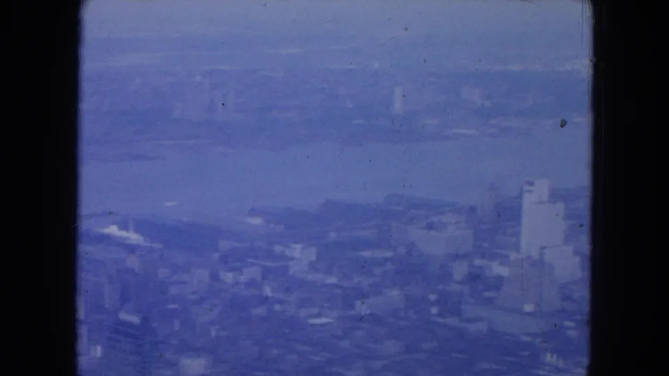 1954 New York City aerial view with a pale high-rise near the waterfront, river beyond, and visible 8mm grain.