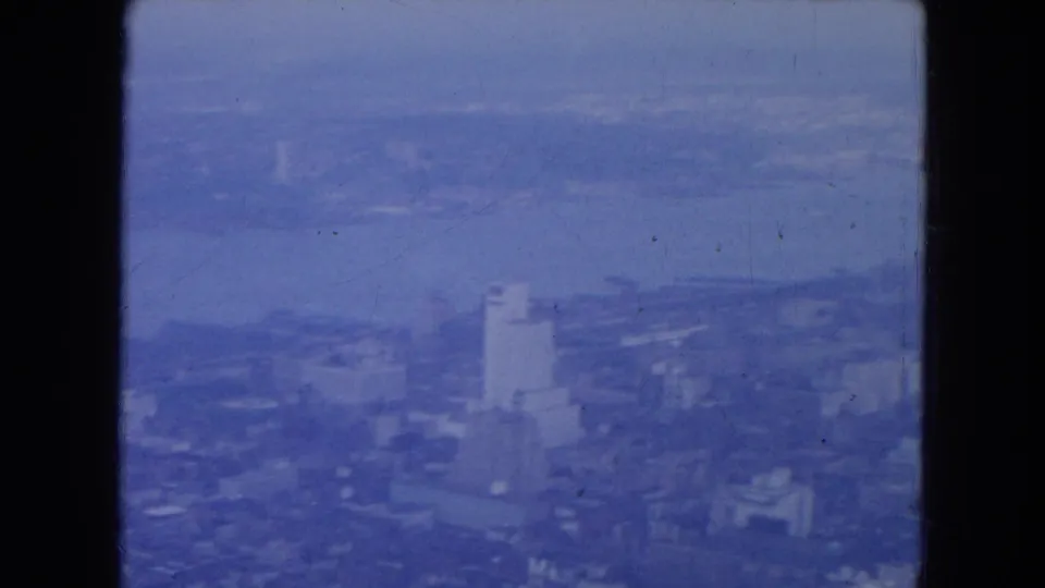 Blue-tinted 1954 New York City aerial frame showing high-rises near the waterfront, river, haze, and film-frame borders.