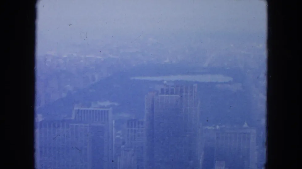 1954 New York City buildings appear below a pale haze, with dark window framing and soft 8mm texture across the scene.