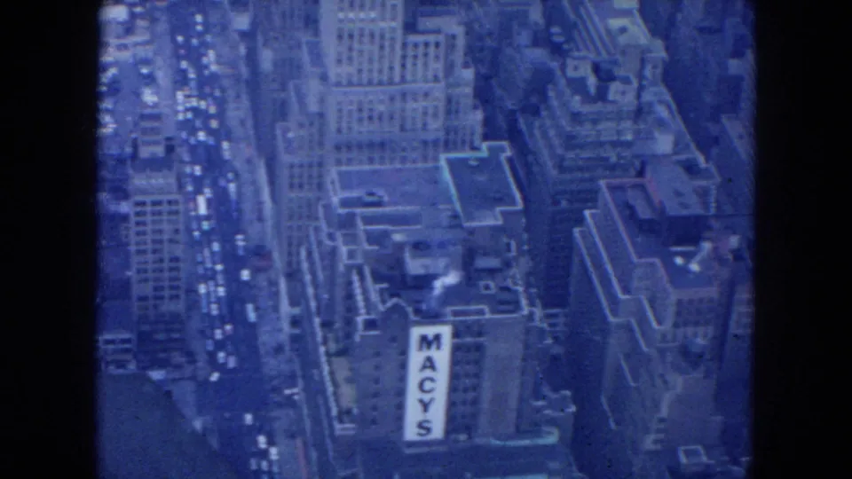1954 New York City aerial frame showing surrounding buildings, traffic, and a visible vertical Macy's sign on one facade.
