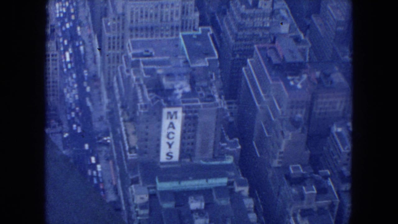 1954 New York City aerial 8mm frame looking down on Midtown buildings, traffic, rooftops, and a large Macy's sign.