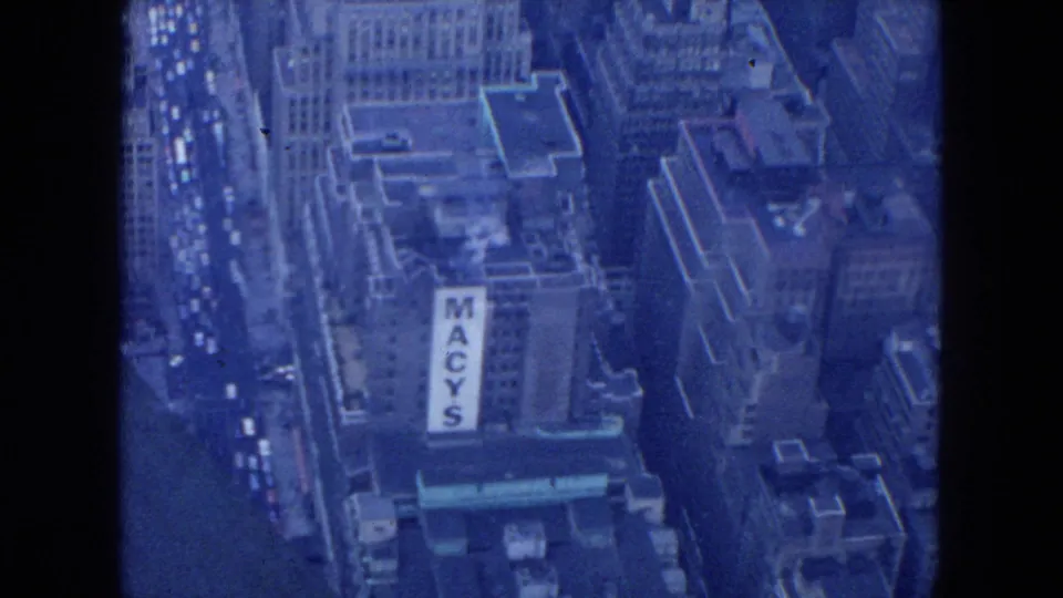 1954 New York City aerial 8mm frame looking down on Midtown buildings, traffic, rooftops, and a large Macy's sign.