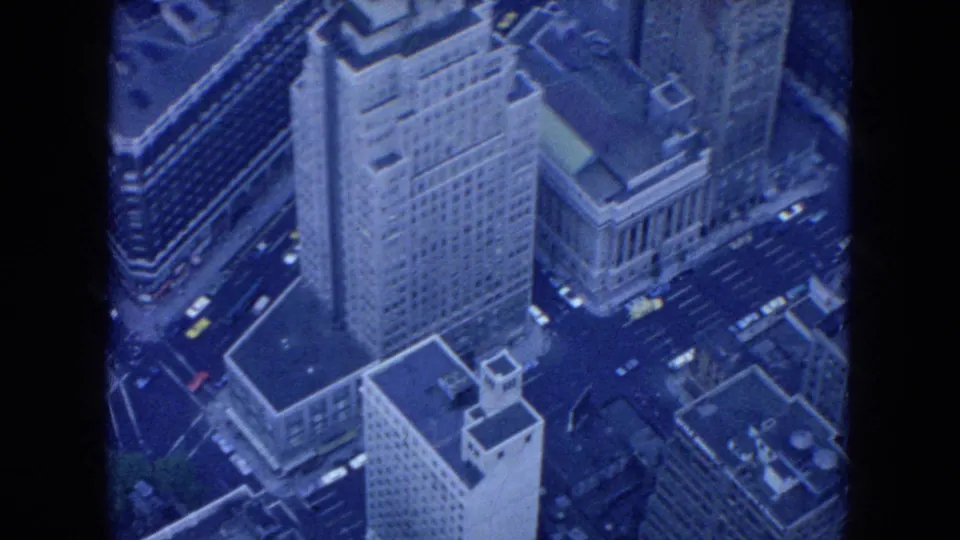 1954 New York City aerial frame looking down on high-rise buildings, rooftops, street lanes, and vintage traffic.