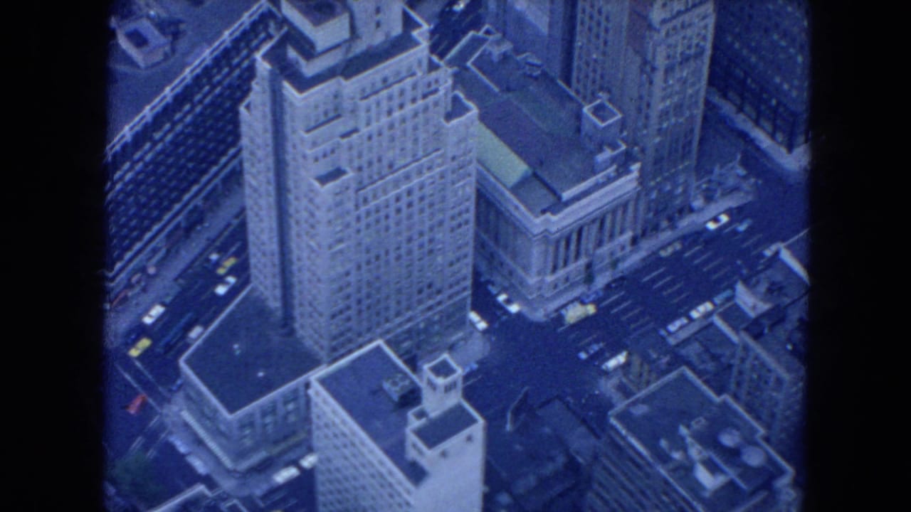 High-angle view of tall city buildings and streets with small cars below.