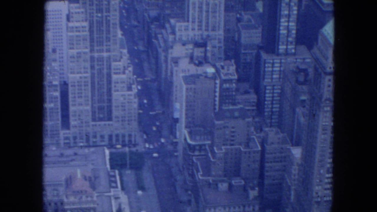 Blue-tinted aerial view of dense skyscrapers and streets between tall buildings.