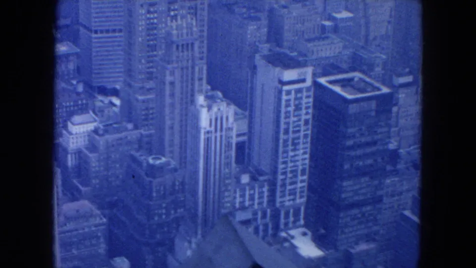 Blue 8mm frame of 1954 New York City high-rises, showing rooftops, facade patterns, and compressed urban blocks.
