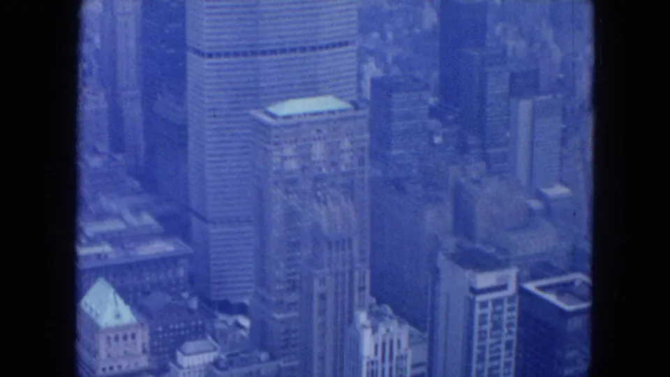 1954 New York City aerial frame with office towers, rooftops, and hazy blue film exposure across the skyline.