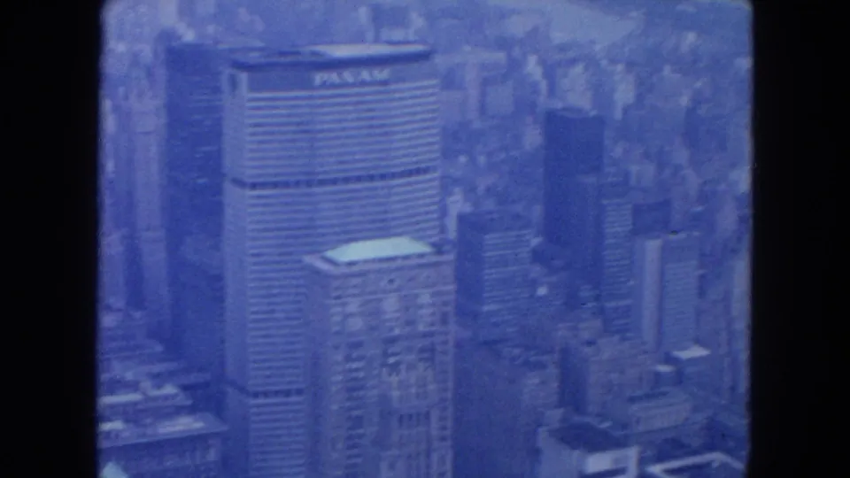 1950s New York City aerial home-movie frame showing dense Manhattan buildings and a visible Pan Am marking through blue-tinted 8mm film.