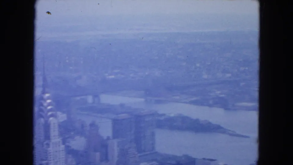 New York City skyline frame showing the Chrysler Building edge, nearby towers, and a broad waterway beyond the city.